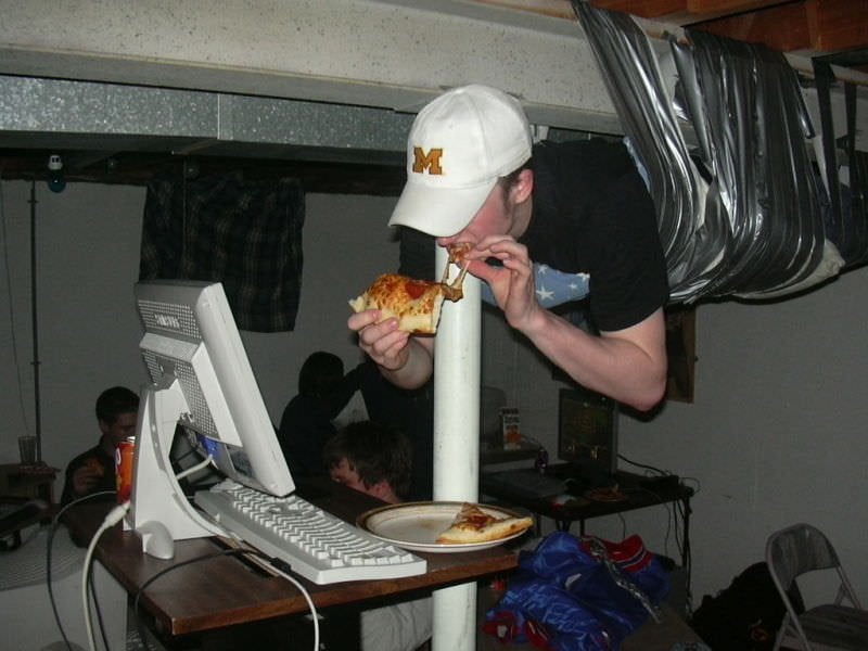 A guest leaning over a desk to eat pizza at a past LAN party